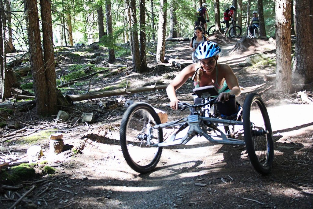 a girl in a handcycle rips down an accessible mountain biking trail