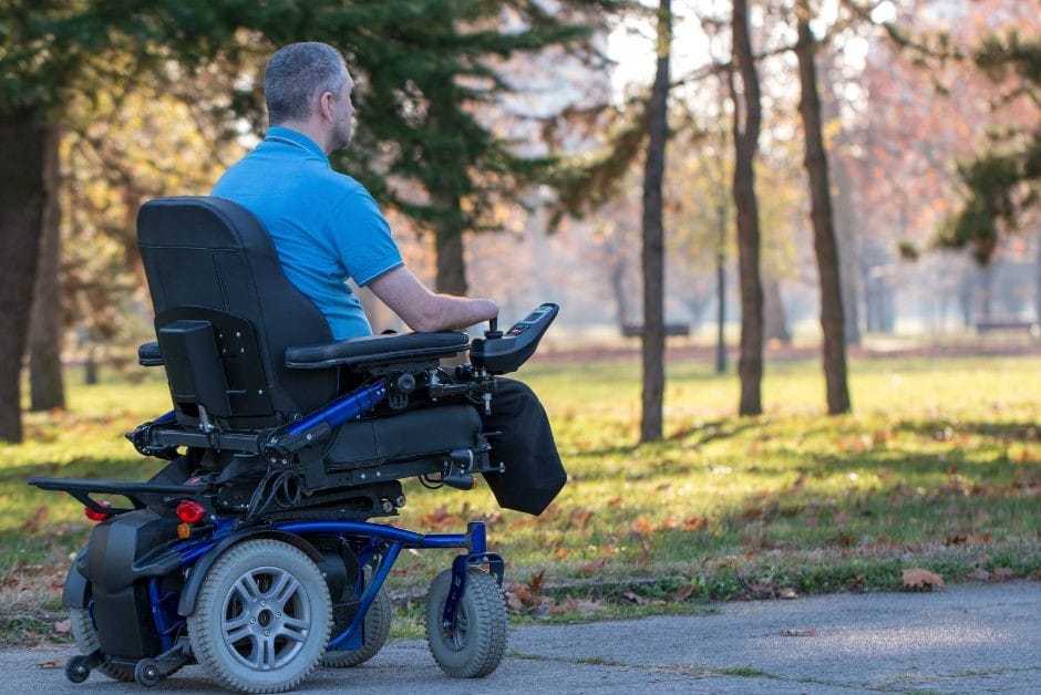 A man in a blue shirt wheeling through a park in his power chair.